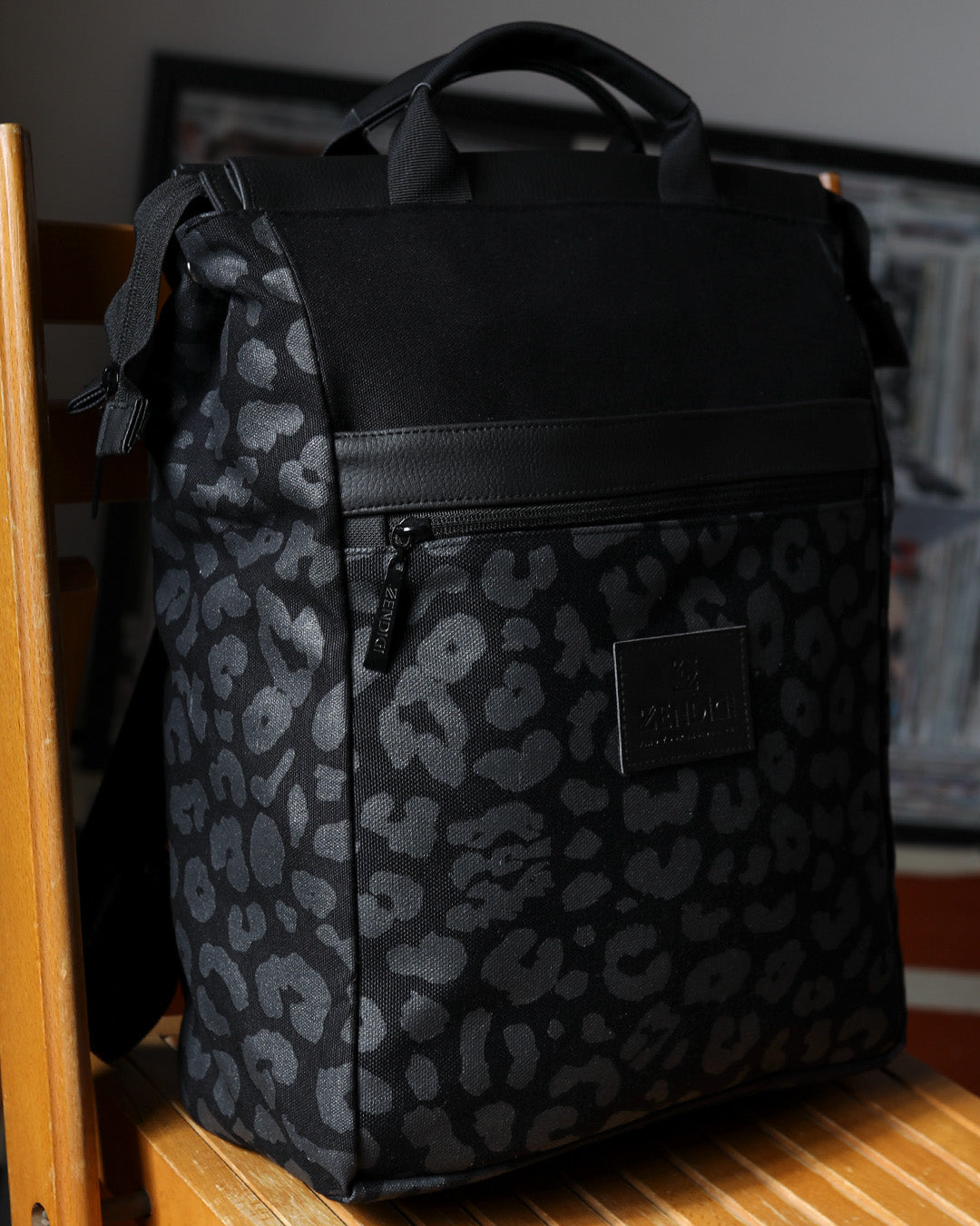 תיק גב מילאנו שחור מנומר למחשב נייד 16 אינץ', מונח על כיסא עץ, עם לוגו ZENDIGI ובהדפס רשת ידני.